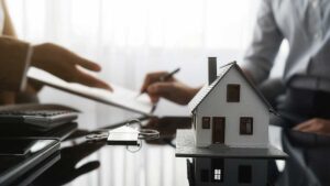 A person takes photos of storm damage to their house and roof using a smartphone while holding an insurance policy folder.