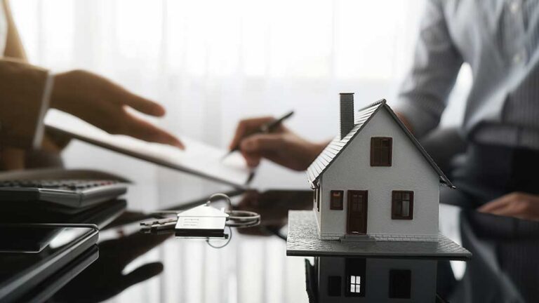 A person takes photos of storm damage to their house and roof using a smartphone while holding an insurance policy folder.